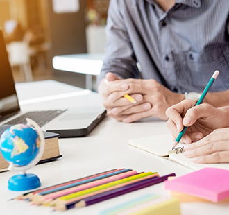 Hands writing in a notebook surrounded by a laptop and school supplies on a table